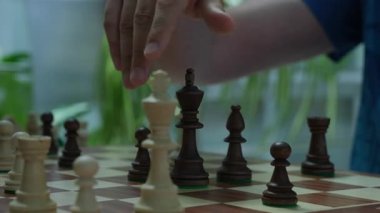 Tişörtlü oyuncu satranç tahtasında King 'in pozisyonunu değiştirmek için hamle kullanır. Odaklanmış adam zamanlayıcıyı durdurur ve satranç oyununda rakibine döner
