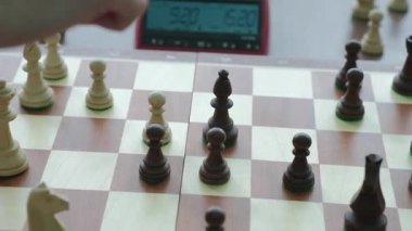Deneyimli satranç oyuncusu, şövalyeyle rakibinin piyonunu yakalar. Satranç tahtasının yakınında yer alan düşünme üzerine harcanan zamanı gösteren saat