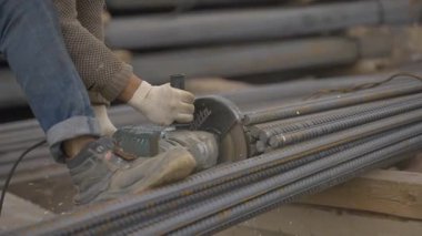 İşçi, çeliği yonga makinesiyle kesiyor ve kıvılcımlar çıkıyor. Metal çubuklar, işlem sırasında istikrarı sağlayan ahşap yüzeyde dururlar.