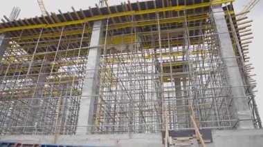 İnşaat sahasında inşa edilmiş yapıyı destekleyen geniş bir yapı iskelesi bulunuyor. Metal iskelet temeldeki beton sütunları kapsar