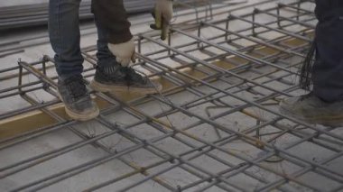 İşçiler çelik takviye çubuklarını sağlam temellere bağlıyorlar. Erkekler yapısal dengeyi sağlamak için parmaklıkları birbirine bağlamak için metal tel kullanıyorlar