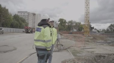 Yüksek görüşlü ceketli ve kasklı inşaat işçileri olay yerinde bekliyor. Erkekler inşaat alanına bakarken çalışmaların ilerlemesini engelliyor