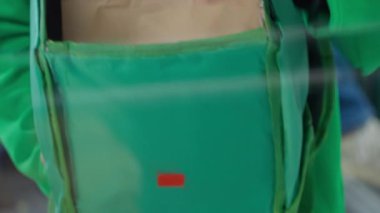 Teslimat işçisi, yiyecek dolu kağıt torbaları almak için çantayı açar ve daha sonra yakın plan çekimler yapar. Düzgün bir rutin yemeğin sıcak ve güvenli kalmasını sağlar.
