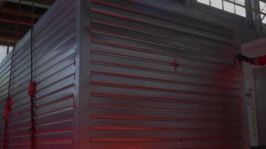 Fabrika atölyesinde işçilerin dikkatle kontrol ettiği kayışlarda bulunan devasa metal konteynırlar. İşlem mekanik güç ve kesinliğin altını çizer