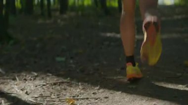 Formda atlet bacakları orman yolunda güçlü bir şekilde koşar. Spor meraklılarının kararlı adımları sessiz orman ritmiyle birleşir.