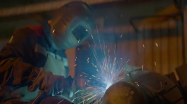 Güvenlik maskesi takan kaynakçı garaj atölyesindeki metali eritiyor. Yetenekli dokunuşlar altında parlayan metal fitiller ve parlak kıvılcımlar uzman ustalığı işaret ediyor.