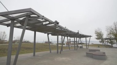 Metal çerçeve ve bulutlu gökyüzüne karşı dairesel delikli paneller ile mimari yapı otobüsü durağı. Tasarım sokak lambalarıyla modern estetik içeriyor