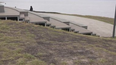 Göle doğru uzanan çimenli yamaç boyunca çok katmanlı ahşap yürüyüş alanı. Tasarım, yürüyüş için eğlence alanındaki platformu göstermeyi öneriyor