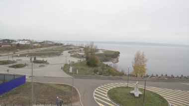 Bulutlu gökyüzünün altında, geniş bir su kütlesinin yanında gezinin. Alanda, dinlenmek için kamusal alan gösteren asfalt yollar sokak lambaları ve yeşillikler yer almaktadır