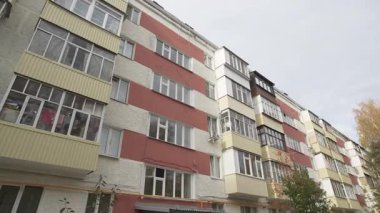 Çok katlı apartman binası. Gökyüzü altında renkli yüzler, tekrarlayan pencereler ve balkonlar var. Kentsel ayar içindeki yerleşim alanı