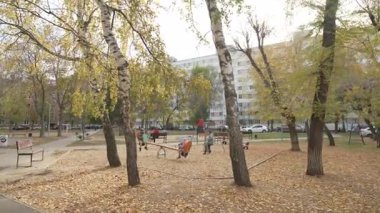 Kentsel yerleşim alanı içinde yer alan parkta kumlu oyun alanı ve çok katlı bina bulunuyor. İnsanların sıcak sonbahar gününün tadını çıkardığı bir an.