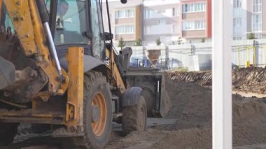 ALMATY, KAZAKHSTAN - 19 Mart 2025: Kazıcı geriye kalan toprağı tekerleklerle düzleştirirken tersine döner. Süreç, inşaata hazırlanmak için zeminin pürüzsüz olmasına yardımcı olur