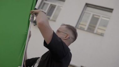 ALMATY, KAZAKHSTAN - AĞUSTOS 05 2024: Mürettebat yeşil ekranı tripoda emniyete aldı. Daha sonra düzenlemek için panel temel oluşturur. Kumaş dikey olarak gerildi ve hizalandı