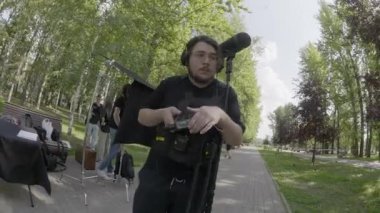 ALMATY, KAZAKHSTAN - AĞUSTOS 07 2024: film çekimi. Ses teknisyeni kayıt cihazını tutuyor ve mikrofon seviyelerini izliyor. Adam kulaklık takıyor ve film setindeki ses ekipmanlarını ayarlıyor.