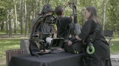 ALMATY, KAZAKHSTAN - AĞUSTOS 07 2024: film çekimi. Ekip dışarıda çekim yapmak için karmaşık kamera donanımı hazırlıyor. Film teknisyenleri, orman bölgesinde masayı hazırlamak için toplandılar.