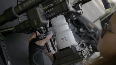 ALMATY, KAZAKHSTAN - AĞUSTOS 07 2024: film çekimi. Genç kadın sinema kamerasını ayarlıyor. Teknisyen odaklanmayı ve işçi yardımı ile ayarları kontrol ederken kamera lensi döner