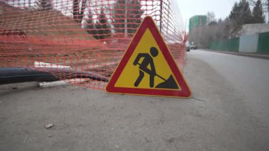Kauçuk boru, parlak trafik tabelasına göre yerden deliğe doğru esiyor. Soğuk havada kaldırım boyunca ilgisiz yayalar geçer.