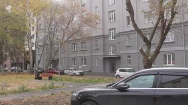 Apartman dairesi küçük ve rahat avluya bakıyor. Sonbahar sarı ağaçları ve park halindeki arabalar sakin bir mahalle havası yaratıyor.