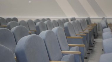 Yumuşak kumaşlı döşeme koltukları düzgün sırada dizilmiş. Tahta kolluklar, öğrenciler için yeni inşa edilen toplantı salonundaki her koltuğu bölüyor.