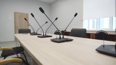 Ahşap konferans masasında birkaç mikrofon var. Çağdaş toplantı alanını saran sandalyeler görüşmeler ve sunumlar için hazır