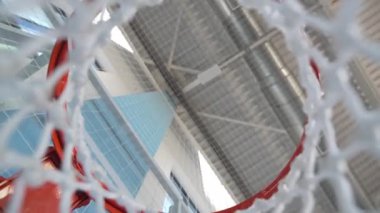 Basketbol potası, çelik tavanı ve modern spor salonu mimarisinin üzerinde görünen geniş pencereleriyle aşağıdan net bir şekilde görülür.