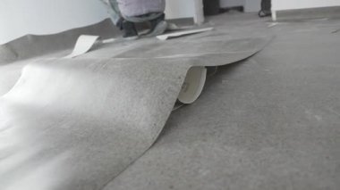 Kişi duvarın yanında diz çökerken vinil çarşaf kabarık zeminde yatıyor. İnşaat, yumuşak gün ışığıyla dolu sessiz bir alanda devam ediyor.