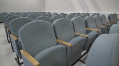Ahşap kollukları olan yumuşak gri sandalyeler uzun sıralar halinde diziliyorlar. Düzenli düzen, organize tasarım ve yapılandırılmış montaj salonu alanını vurgular