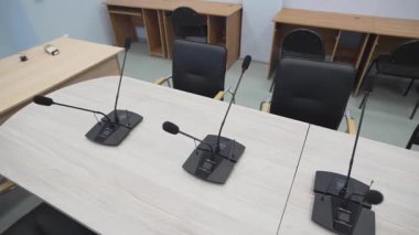 Konferans odasında boş sandalyeler ve yeni mikrofonlar var. Modern ofis kurulumu profesyonel ekipmanlarla resmi toplantıya hazırlanıyor