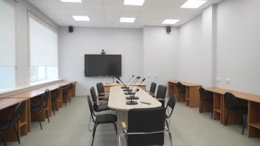 Konferans odasında mikrofonlar ve büyük ekranlı modern toplantı masası yer alıyor. Sandalyeler ve masalar iş iletişimi için hazır.