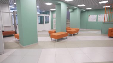 Canlı koltuklar açık renkli sütunların yanında durur. Lobide parlak tavan ışıkları parlıyor. Resepsiyon alanı boş salonda modern ve temiz görünüyor.