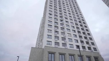 Aydınlık cepheli ve eşit aralıklı sayısız pencereli uzun, modern konut binası. Yapılar bulutlu gökyüzünün altında yüksek katlı binaların yanında etkileyici yükseklikte.