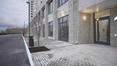 Binanın modern girişi. Kaldırımın yanında ışık var. Beton duvarları ve konut kompleksinde geniş pencereleri olan yüksek binalar.