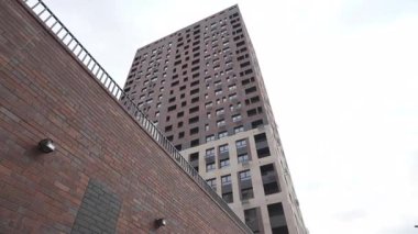 Düşük açılı modern tasarımı olan yüksek katlı bir bina. Metal parmaklıklı tuğla duvar derinlik ve kontrastlık hissi yaratıyor