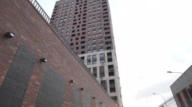 Bulutlu gökyüzü alçak açılı çekim altında çağdaş tasarımı olan yüksek konut binası. Metal parmaklıklı tuğla cephesi olay yerine derinlik ve kontrastlık ekler