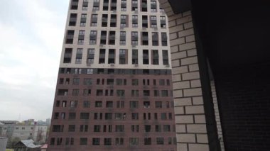 Bulutlu gökyüzünün altında aydınlık ve karanlık yüzleri olan uzun gökyüzü düzenleyicisi. Tamamlanmamış inşaatın tuğla balkonundan sayısız penceresi olan modern bina.