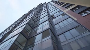 Yüksek katlı cam balkonlar alçak açılı temiz gökyüzüne karşı duruyor. Konut kompleksi içinde koyu kırmızı cepheli uzun modern bir bina.