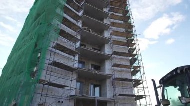 Tamamlanmamış ofis kulesi, rüzgarda gürültülü bir şekilde çırpınan eski püskü muşambaları giyiyor. Sert şapkalı işçiler metal iskeletlerde ihtiyatlı hareket ediyorlar.