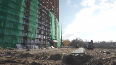 Geniş inşaat alanında beton yapıyı çevreleyen derin kumlu siperler vardır. Kazıcılar yeni kazılmış toprak yığınlarının yakınında boş boş otururlar.