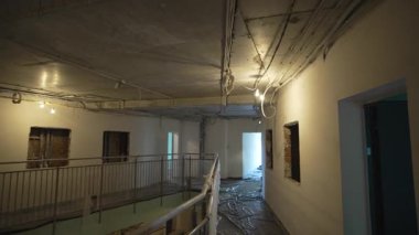 Küçültülmüş raylar çiğ beton levhaların kenarlarında uzanıyor. Geçici inşaat aydınlatması dekore edilmemiş duvarlar boyunca uzun gölgeler bırakıyor.