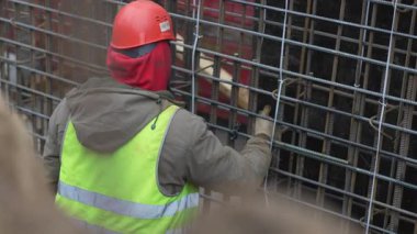 Miğferli miğfer, inşaat demiri ızgarasını dikkatlice ayarlar. Eller yapısal temeller için çerçeve şekillendirir. Demir yerleştirme güç ve denge yaratır