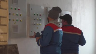 Elektrikçiler güç panelini açıp telefondaki içeriği kaydediyorlar. Görüntü dökümanları açık paneldeki kablolama düzeni. Erkekler devre düzenini izler