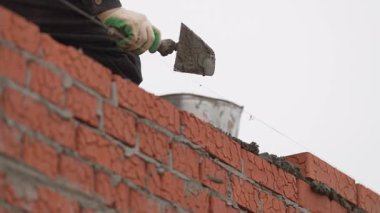 Gri çimento kırmızı tuğla sırasına yayılmış. Yapışkan yüzey inşaat için hazır. Mason bir sonraki kat için düz taban inşa ediyor.