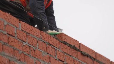 İnşaatçı tuğla pozisyonunu ayarlarken keskin malayla betonu temizliyor. Deneyimli mason, temiz hatları etkili bir dokunuşla şekillendirir.