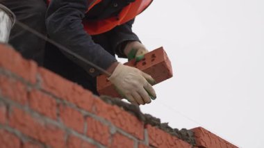 Eldivenli ve kasklı işçiler yeni tuğlaları sıraya diziyor. Taze çimento belli bir hizada yapışır. Tuğlacı kontrolü duvarı mükemmelleştirir