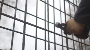 İnşaatçı inşaat alanındaki metal çubuk ızgaralarını birbirine bağlıyor. Eldiven giyen işçiler çit çerçevelerini dışarıda demirlerle birleştiriyor