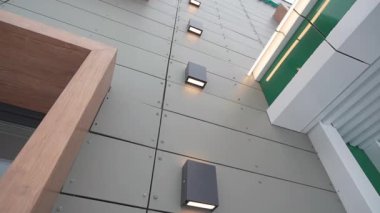 Akıllı lambalar modern binanın ön cephesinde, alçak açılı çekimde parlıyor. Caddedeki kamu merkezinin dış tarafında dizilmiş minimalist ışık noktaları