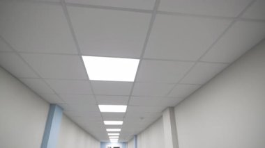 Hastane koridorundaki asılmış tavanda kare şeklinde lambalar parlıyor. Parlak verimli aydınlatma ekipmanları kamu binasında yolu aydınlatıyor