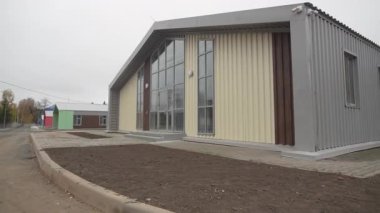 Bulutlu gökyüzünü yansıtan panoramik pencereli tek katlı bir konak. Temiz modern hatlar, sessiz komşuluk duygusunu arttırır.