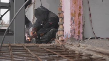 Kaynakçılar gökyüzünün altında güçlü bir çerçeve oluştururken kıvılcımlar çakıyor. Demir kirişler kızgın bir yoğunlukla parlarken insan zırhlı maskenin içinden odaklanıyor.