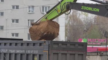ALMATY, KAZAKHSTAN - 17 Ekim 2024: şehir caddesindeki kepçe kepçesinden kamyon römorkuna toprak dökülüyor. Kazıcı, şehir bölgesindeki kamyona fazla toprak yüklüyor.